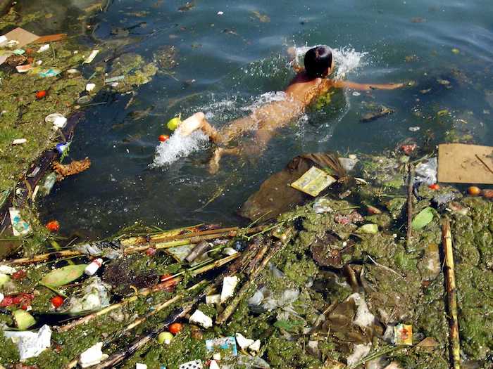 A boy swimming in a garbage-filled pond